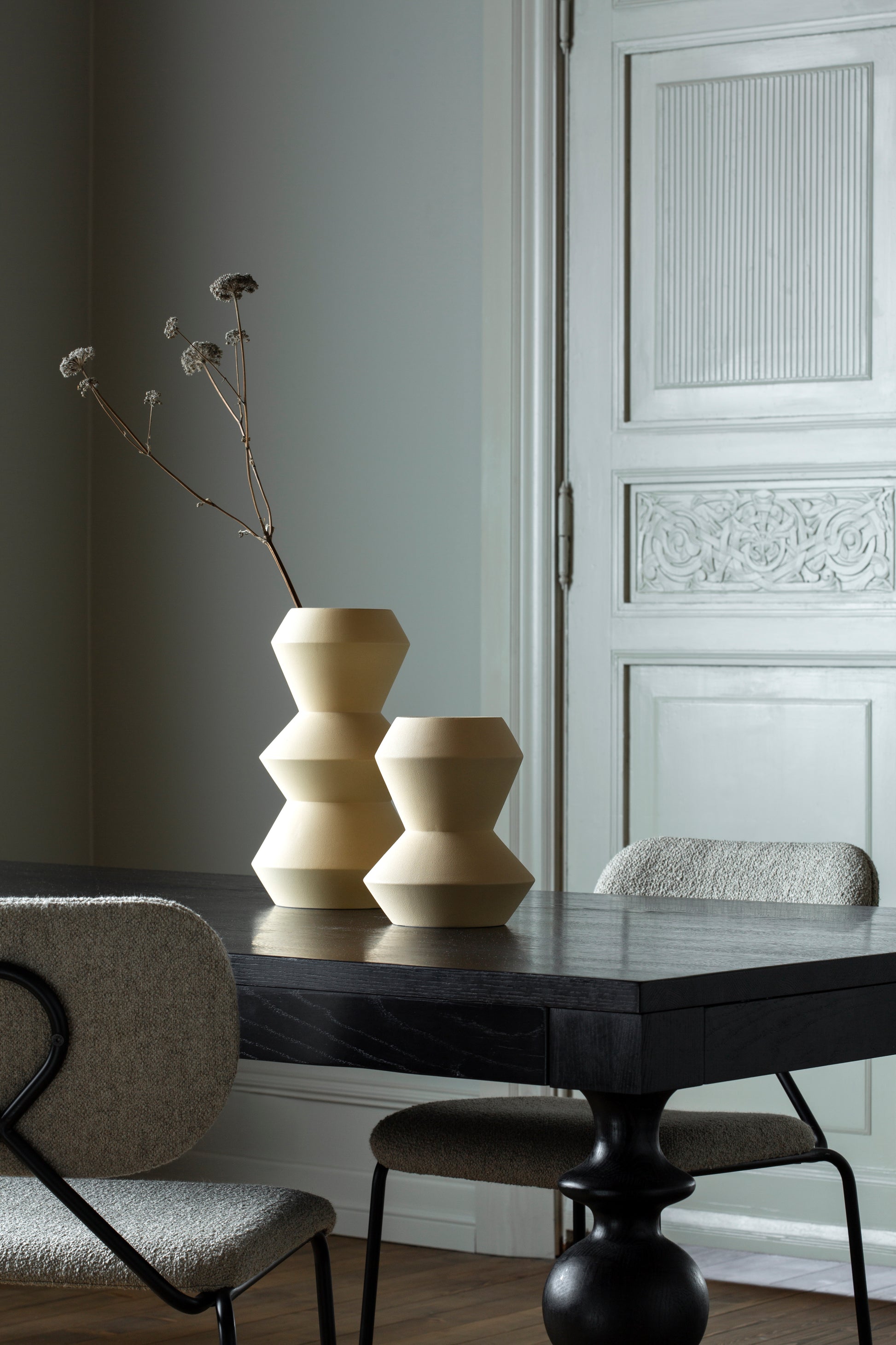 Dia vase 22 og 34 centimeter fra ygg&lyng i fargen straw yellow på et svart oljet viola bord med løkke stoler.